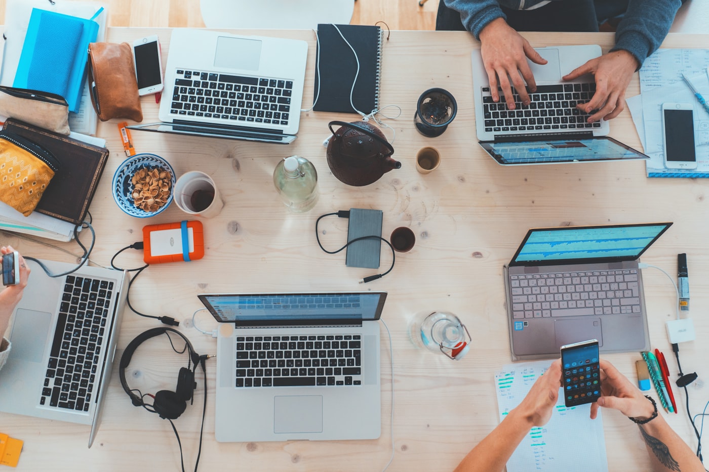 A shared desk seen from above: laptops, notebooks, and coffee mid-workday.