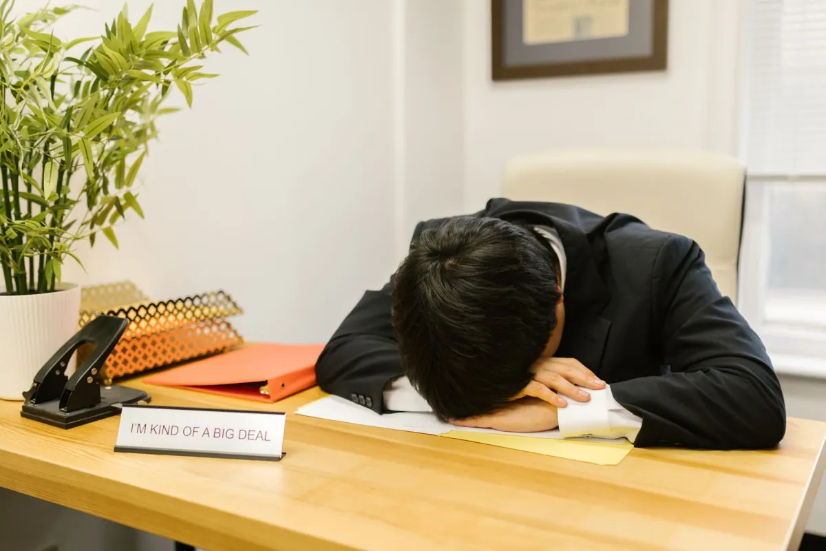 Business professional in suit asleep at desk in office environment.