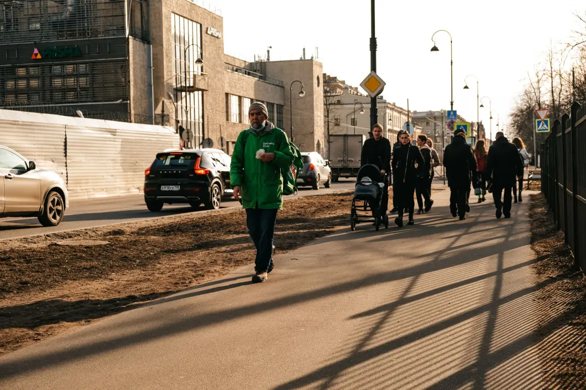 Busy city sidewalk with pedestrians and cars on a sunny day.