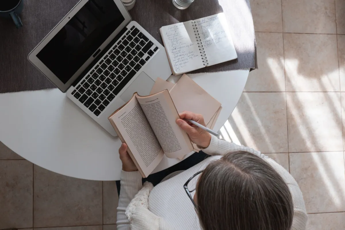 Overhead view of a woman studying with a laptop and open book on a table, creating a productive atmosphere.